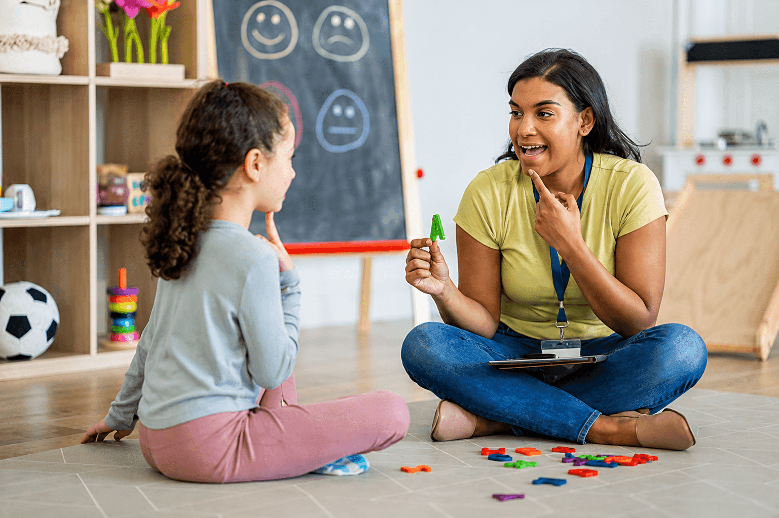 A speech-language pathologist holding a letter tile while working with a young patient on articulation